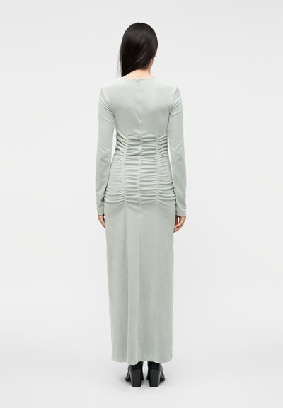 Mintno zelena obleka z dolgimi rokavi, ki ima nabrane detajle na hrbtni strani in raven rob, izdelana iz mehke tkanine.