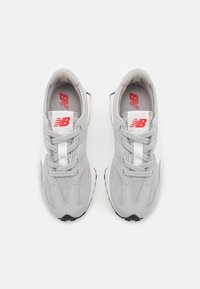 Chaussures de sport grises avec une tige en maille et en daim, lacets blancs et un logo rouge sur la languette. Semelle extérieure noire avec des détails texturés.