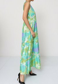 Robe maxi avec un motif aquarelle vert et bleu, design en couches, accents en dentelle et bretelles spaghetti, associée à des chaussures à talons hauts noires.