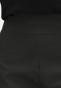 Zwarte high-waisted broek met een gladde textuur en schone naden. De stof lijkt rekbaar met een matte afwerking.