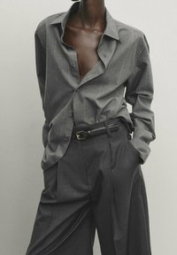 Chemise gris rayée avec un col ouvert, associée à un pantalon gris taille haute et une ceinture noire. Tissu lisse, coupe décontractée.