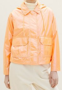 Giacca corta, con cappuccio, lucida di colore arancione chiaro con due tasche frontali. Il materiale sembra liscio e leggero.