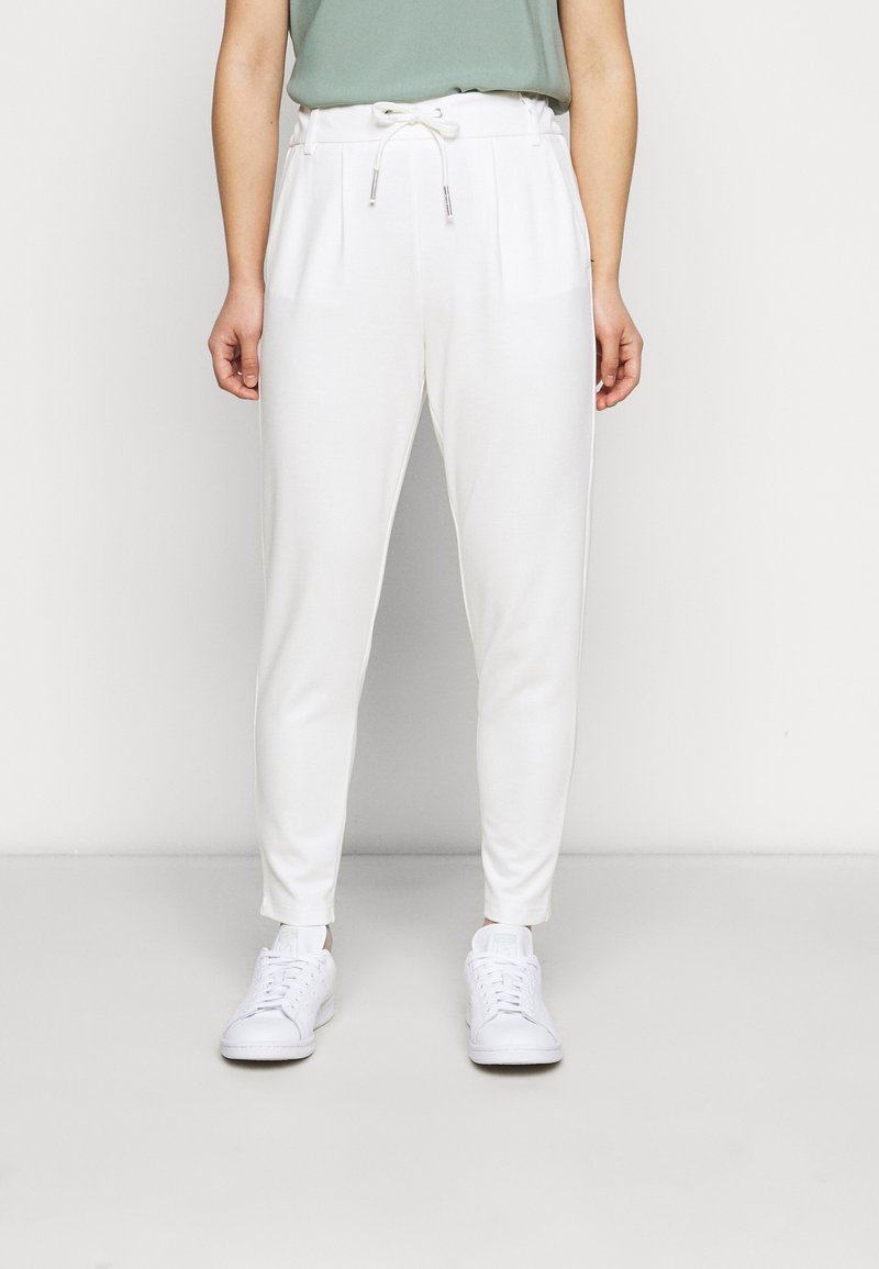 Bílé tapered tepláky s elastickým pasem a šňůrkou, mají boční kapsy a hladkou látku, doplněné o bílé tenisky.