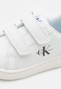 Witte sneakers van synthetisch leer, met een dubbele klittenbandsluiting, geborduurd logo en een ronde neus.