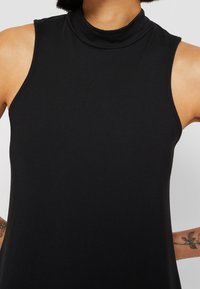 Černý bezramenný top s vysokým výstřihem vyrobený z měkké tkaniny, který se vyznačuje hladkým povrchem a minimalistickým designem, odhalující oblast výstřihu a ramen.