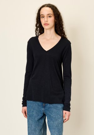 Schwarzes Langarm-V-Ausschnitt-Oberteil aus leichtem Stoff mit lockerem Schnitt und gerippten Bündchen, kombiniert mit hellblauen, hoch taillierten Jeans.