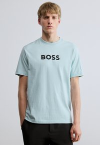 Hele sinine lühikeste varrukatega puuvillane T-särk, ümmarguse kaelusega ja esiküljel must "BOSS" logo. Lihtne, siledapinnaline tekstuur.