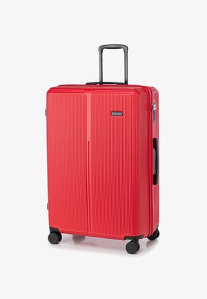 Red hard-shell suitcase with vertical ribbed texture, retractable handle, and four black wheels. Features a logo on front.