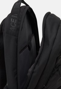 Sac à dos noir avec compartiment principal partiellement ouvert montrant une poche intérieure pour manchette et une sangle de poignée supérieure.