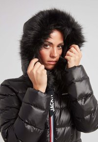 Czarna kurtka puchowa z kapturem obszytym futrem, z zapięciem na zamek, poziomym przeszyciem oraz markowym paskiem na uchwycie zamka.