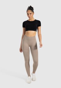 Zwarte korte mouwen crop top en beige hoge taille leggings van rekbaar materiaal, gedragen met witte sneakers. Gladde textuur, aansluitend ontwerp.