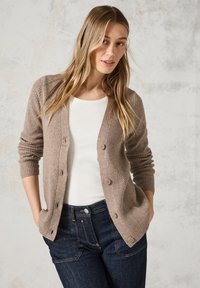Cardigan beige a costine con scollo a V, caratterizzato da sei bottoni e maniche lunghe, indossato sopra un top bianco e jeans in denim scuro.