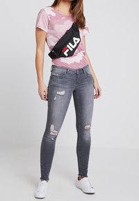 Růžový maskáčový tričko, černý ledvinko značky Fila, šedé potrhané skinny džíny a bílé tenisky. Neformální, dobře padnoucí outfit s zdrsněnými detaily.