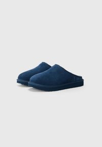 Chaussons en daim bleu marine, à enfiler, avec un bout rond, une surface texturée et une semelle épaisse antidérapante. Pas de matériel ou d'accents visibles.