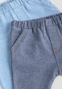 Deux paires de pantalons doux et extensibles : une bleu clair, une bleu foncé. Les deux ont des taille élastiques et une poche sur le côté de la paire bleu foncé.