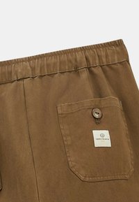 Shorts marron en tissu lisse. Dotés d'une taille élastique et d'une poche à rabat avec un bouton et une étiquette.