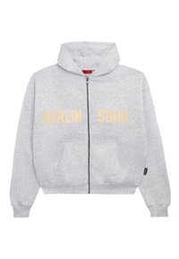 Felpa grigia con zip, realizzata in tessuto morbido, con grande scritta beige "BERLIN SOHO" sul davanti e una tasca a marsupio.