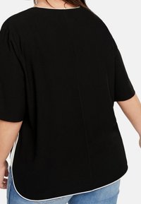 Haut noir à manches courtes avec un col rond, un subtil passepoil sur les côtés et une coupe décontractée, fabriqué dans un tissu lisse avec un dos légèrement plus long.