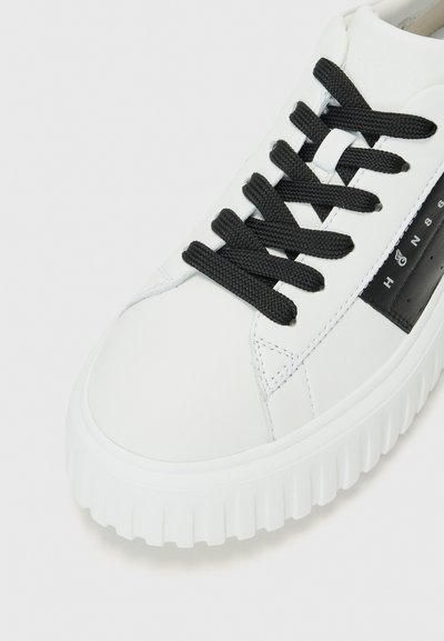Baskets blanches avec une semelle épaisse, lacets noirs et un panneau d'accent noir sur le côté. Matériau en cuir lisse avec des détails cousus.