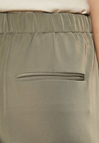 Olijfgroene broek met een soepele textuur, voorzien van een elastische tailleband en een discreet geplaatst achterzakje.