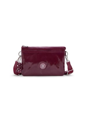 Sac à bandoulière en cuir verni bourgogne avec une fermeture éclair, détail de logo circulaire et un charm amovible sur la sangle. Texture lisse.