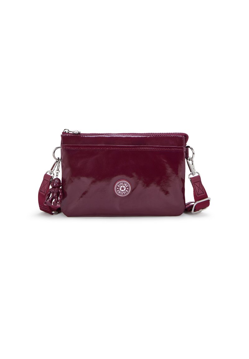 Sac à bandoulière en cuir verni bourgogne avec une fermeture éclair, détail de logo circulaire et un charm amovible sur la sangle. Texture lisse.