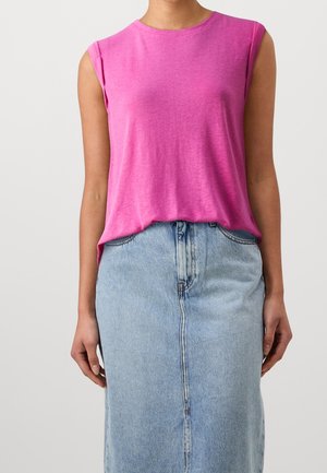 Kvinde iført en ærmeløs, knaldrød top stoppet ned i et høj-taljet, lyseblåt denims nederdel, stående mod en ensfarvet baggrund.