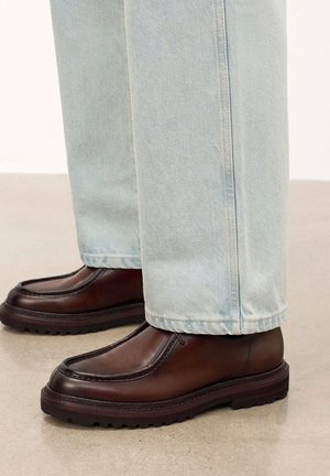 Zapatos de cuero marrón con punta redonda y costuras visibles, combinados con unos vaqueros de mezclilla azul claro de corte recto y dobladillo.