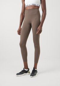 Högmidjade bruna leggings tillverkade av ett elastiskt material, med platta sömmar och en diskret Nike-logotyp på underbenet.