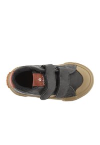 Zapato de cuero gris con dos correas de velcro, suela de goma beige y una pequeña etiqueta de acento roja. Textura suave con punta reforzada.