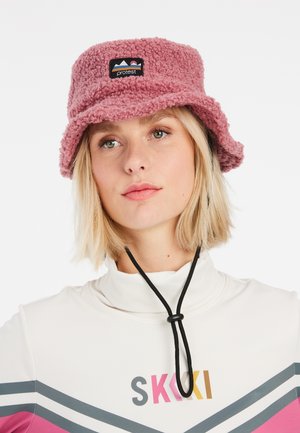Roze pluche emmerhoed met een logo-opdruk, voorzien van een zachte textuur en een zwarte verstelbare kinband. Draagt met een witte top met hoge kraag.