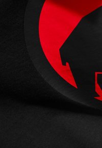 Sort stof med et cirkulært rødt grafik, der har en sort silhuet af et hus og et lyn, hvilket understreger den markante farvekontrast.