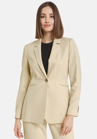 Beige blazer made of smooth fabric, featuring a notched lapel, single button closure, two front pockets, and subtle seam detailing.