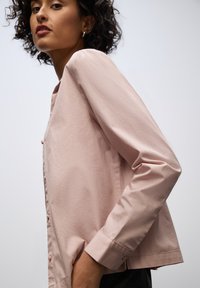 Chemise boutonnée rose clair à manches longues, avec une texture douce et lisse et un éclat subtil, conçue dans une coupe décontractée.