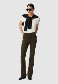 Biały top z krótkim rękawem w połączeniu z oliwkowozielonymi rozszerzanymi spodniami z przodu zapinanymi na guziki. Czarny sweter narzucony na ramiona; ciemne okulary przeciwsłoneczne.