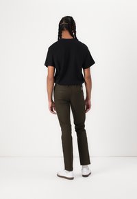 Sort kortærmet t-shirt parret med olivengrønne tætsiddende bukser og hvide sneakers. Outfitet har et afslappet design med en enkel silhuet.