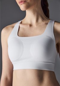 Hvit sports-BH med brede stropper, jevn tekstur og formede kopper. Har en sømløs design og en tettsittende elastisk underbånd.