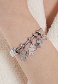 Zilveren bedelarmband met meerdere hangers, waaronder twee figuren, een cadeaubox en een balletdanseres, met kristallen en een glanzende afwerking.