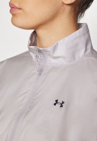 Light purple, lightweight windbreaker with a stand collar, front zipper, and black logo on the chest; features a textured fabric pattern.