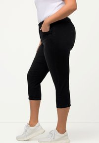 Pantalones cortos negros de mezclilla, con un diseño ajustado y bolsillos estándar. Llevados con zapatillas blancas para crear contraste.
