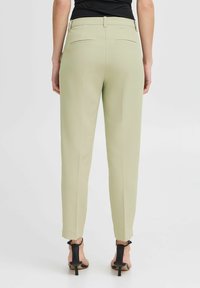 Svetlozelene krojene hlače z gladko teksturo, z zadnjimi žepi in ožjim krojem, v kombinaciji s črnimi sandali s peto.