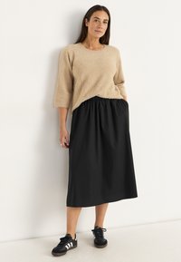 Beige textured sweater with three-quarter sleeves paired with a black ankle-length skirt featuring an elastic waistband and black sneakers.