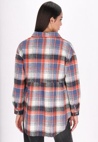 Checkered flannel shirt in red, blue, and white colors, featuring a collared neckline, long sleeves, and a gathered back design.
