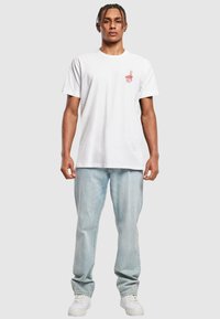 T-shirt en coton blanc avec un petit graphique rouge d'une boîte à emporter sur la poitrine gauche, associé à un jean en denim bleu clair et des baskets blanches.