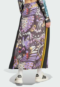 Maxi skirt with butterfly print in purple, black, and yellow; features a drawstring waistband and side stripes. Paired with white sneakers.
