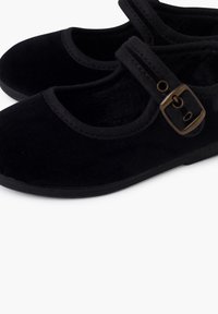 Scarpe Mary Jane nere con una sola cinghia e fibbia bronzata, realizzate in un materiale morbido simile al velluto, presentate su uno sfondo bianco.