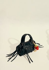 Black leather bag with braided handles, two zippers, and long fringes. Features a colorful keychain with a crochet strawberry design.