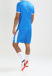 Camisa y pantalones cortos deportivos azules con acentos blancos, con cuello redondo, mangas cortas y diseño de panel lateral. Tejido texturizado y ajuste deportivo.