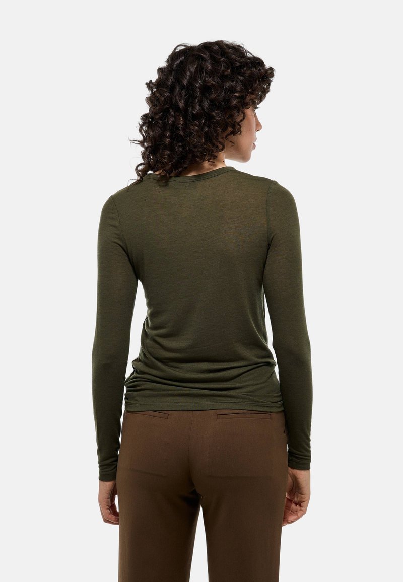 Haut à manches longues olive avec un col rond et une coupe ajustée, associé à un pantalon marron avec des poches arrière. Tissu doux et léger.