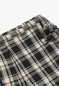 Tissu à carreaux noir et crème avec une taille relaxée et des passants de ceinture. La texture est lisse, avec un motif tissé à rayures alternées.
